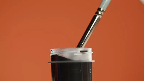 Black paint isolated on orange background. Dark gouache falling from paintbrush Stock-Footage 178594546