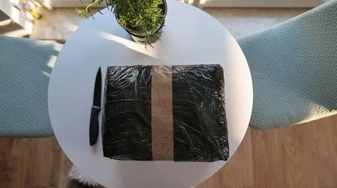Black Parcel Wrapped in Plastic and Tape on a White Table Stock Photos