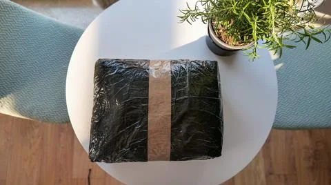 Black Parcel Wrapped in Plastic and Tape on a White Table Stock Photos