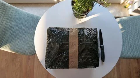 Black Parcel Wrapped in Plastic and Tape on a White Table Stock Photos