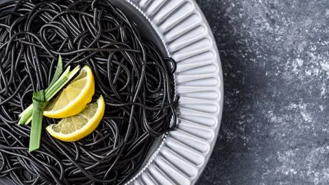 Black paste with ink cuttlefish and lemon slices in gray plate on gray backgr Stock Photos