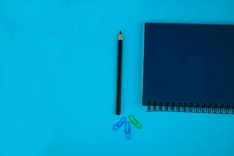A black pencil crayon,three different colored paper clips on a blue backgroun Stock Photos