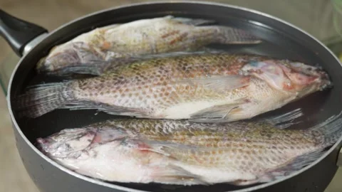 Black person squeezing lemon juice over raw whole tilapia fish Stock Footage 340451656
