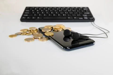Black phone and coins stack with headphones and a keyboard Stock Photos