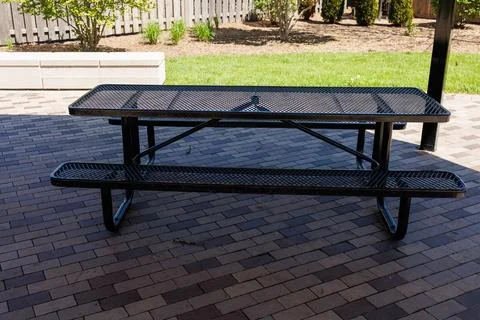 Black picnic table placed on pavement under a shelter in a green yard durin.. Stockfoto's