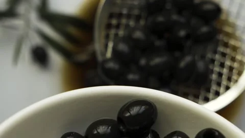 Black pitted olives accumulating in white bowl with skimmer motion on white.. Видео 334332999