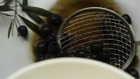 Black pitted olives scooping to white bowl with metal skimmer 4k 120fps Stockbeeldmateriaal 334328247