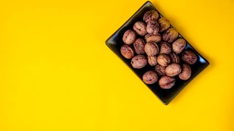 Black plain dish full of nuts on a yellow background. Stock Photos