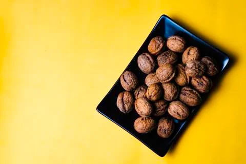 Black plain dish full of nuts on a yellow background. Stock Photos