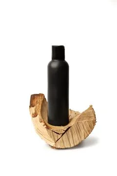 A black plastic bottle on a piece of tree trunk on a white background Stock Photos
