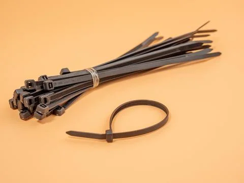 Black plastic cable ties on an orange background. Stock Photos