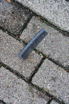Black plastic comb lying on paving tiles in the street Stock Photos
