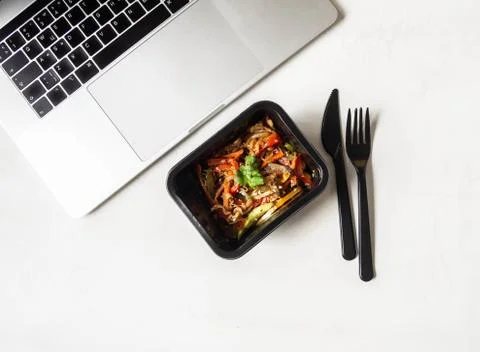 Black plastic container with vegetables stir fry and laptop Stock Photos