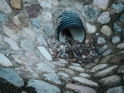 A black plastic drainage pipe embedded in a stone-lined ditch. Stock Photos