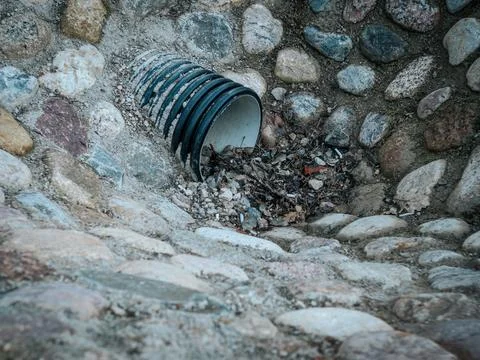 A black plastic drainage pipe embedded in a stone-lined ditch. Stock Photos