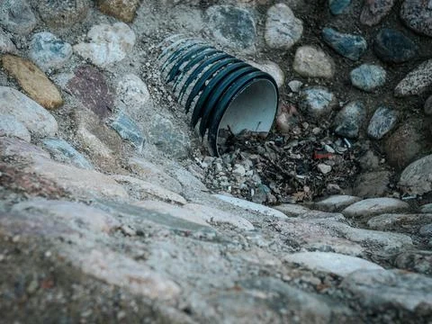 A black plastic drainage pipe embedded in a stone-lined ditch. Stock Photos