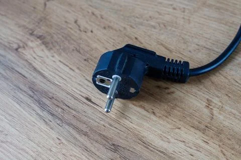 Black plastic electrical plug with metal pins lying unplugged on a wooden t.. Foto stock