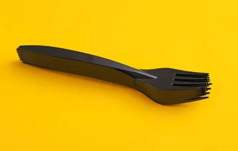 Black plastic fork stacked on yellow background Stock Photos