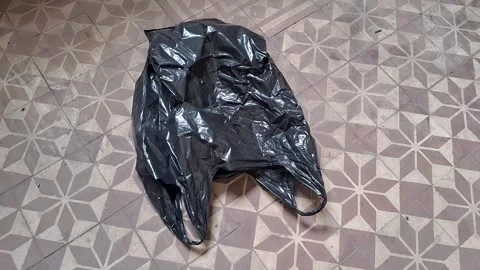 Black plastic garbage bag sitting on patterned floor motion video Stock Footage 339349228