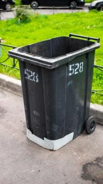 Black plastic garbage collection container on the street with the lid open Stock Photos