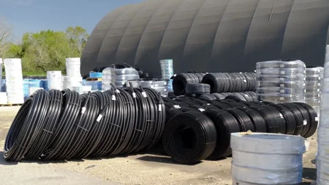Black plastic irrigation pipes coiled in large rolls, stored outdoors in an Stock Footage 340912880