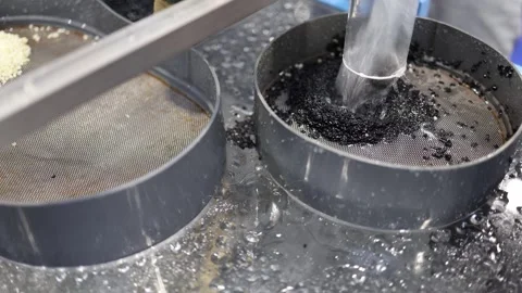 Black plastic pellets rapidly pour through water chute into industrial metal sie Stock Footage 311131002