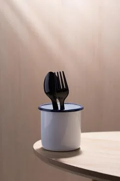 Black plastic spoon and fork in a white enamelware cup. Stock Photos
