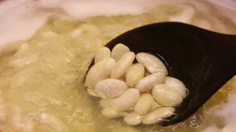 Black plastic spoon mixing boiling water with cooking white beans close up Stock Footage 264966579
