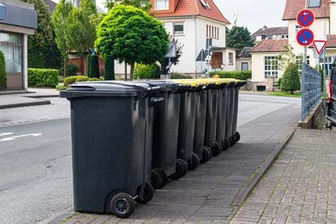 Black plastic trash cans lined up on the sidewalk. Stock Photos