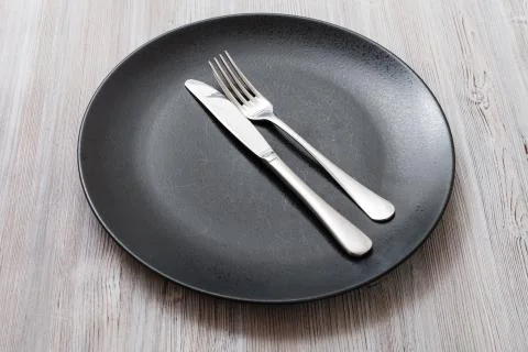 Black plate with parallel knife, spoon on gray Fotos Stock