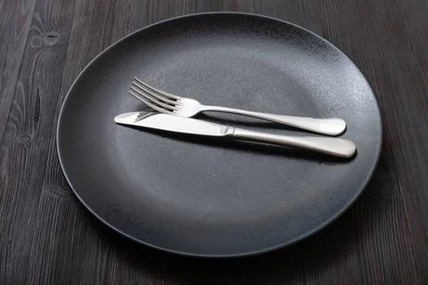 Black plate with parallel knife, spoon on dark food concept - black plate ... Foto stock