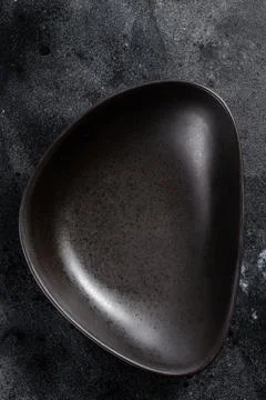 Black plate triangular shape on textured black background. Top view. Copy space 스톡 사진