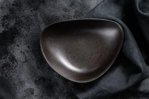 Black plate triangular shape on textured black background. Top view. Copy space 스톡 사진
