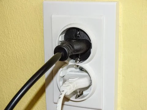 A black plug and a white plug in the socket Stock Photos