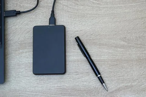 Black Portable External Hard Drive Plugged into Laptop with Elegant Pen Stock Photos
