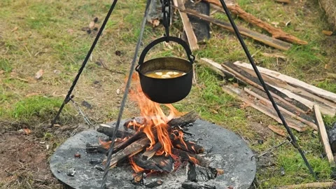 A black pot hangs over an open fire, with flames rising below it. The setup is 스톡 동영상 345037001