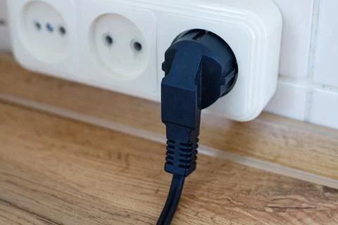 Black power plug inserted into an white electrical socket on a wall backgroun Stock Photos