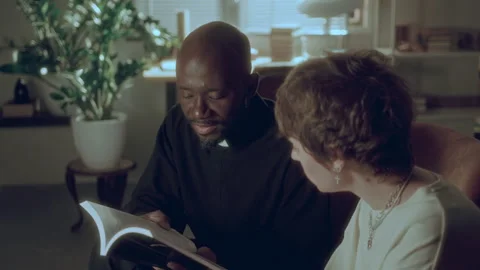 Black Priest Explaining Teachings of Holy Bible to Woman during Home Visit Stock Footage 287764246