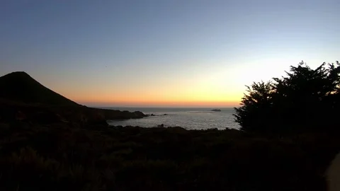 Black profile of plants and mountain with sunset horizon of ocean Stock Footage 143429636