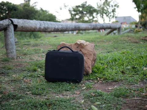 Black protective case on grass next to rock outdoors Stock Photos