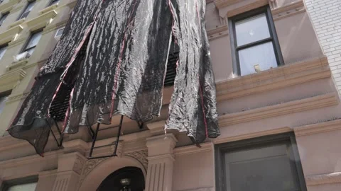 Black protective netting dangles from the fire escapre of a pink brownstone Stock Footage 242365474