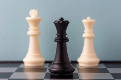 Black queen standing between two white kings on chessboard Stock Photos