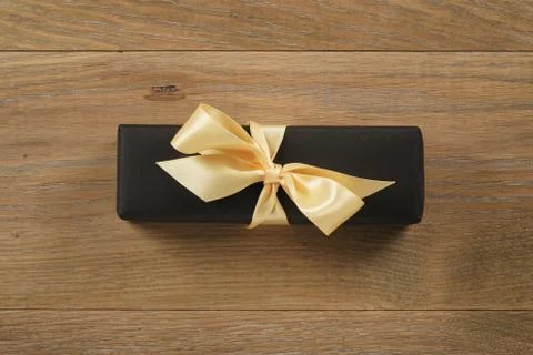 Black rectangle gift box with champagne color ribbon bow on wooden oak table Stock Photos