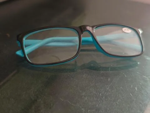 Black Rectangular Eyeglasses with Turquoise Temples on a Reflective Surface 스톡 사진