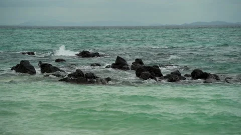 Black reef rocks jut out of the water in the open blue sea Stock Footage 309751590