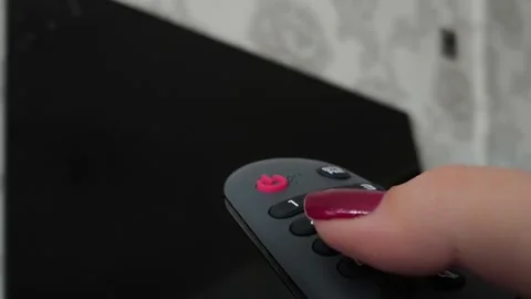 A black remote control in a womans hand against the background of a black TV Stock Footage 318391159