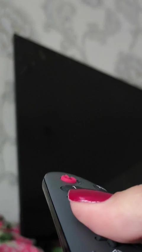 A black remote control in a womans hand against the background of a black TV Stock Footage 318391257