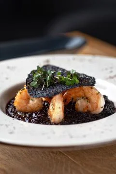 Black rice risotto. Shrimp risotto on a white plate on the table, serving in a Stock Photos