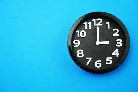 Black round clock showing five o'clock on blue background Foto stock