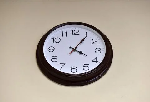 A black round clock with a white dial on a light wall. Stock Photos